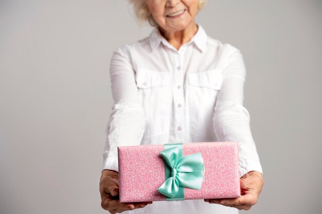 Retrato de foto de anciana curiosa dando caja de regalo y sonriendo aislado sobre fondo gris Concepto de día de la mujer