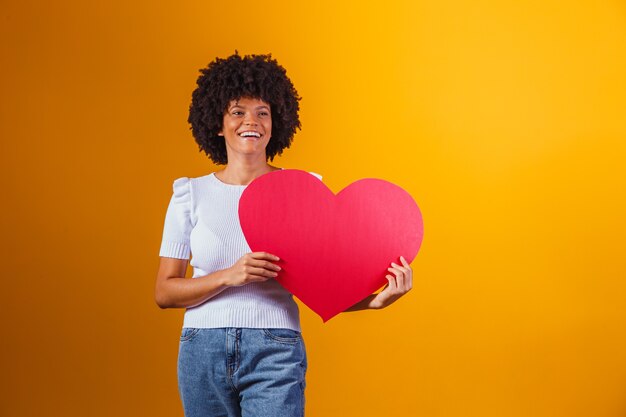 Retrato de foto de mujer afro sonriente sosteniendo una gran tarjeta de corazón rojo