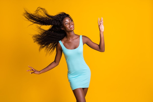 Retrato de la foto de la mujer afroamericana de ensueño con el pelo que vuela viento suave que sopla con un vestido azul aislado sobre fondo de color amarillo vivo