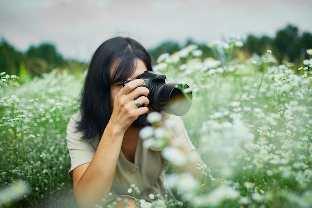 Retrato de una fotógrafa que toma una foto al aire libre en un paisaje de campo de flores sosteniendo una cámara