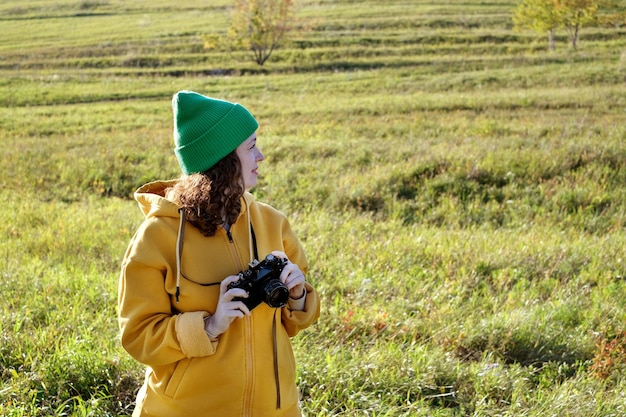 Retrato de una fotógrafa rizada al aire libre. Mujer camina y toma fotos con su cámara.