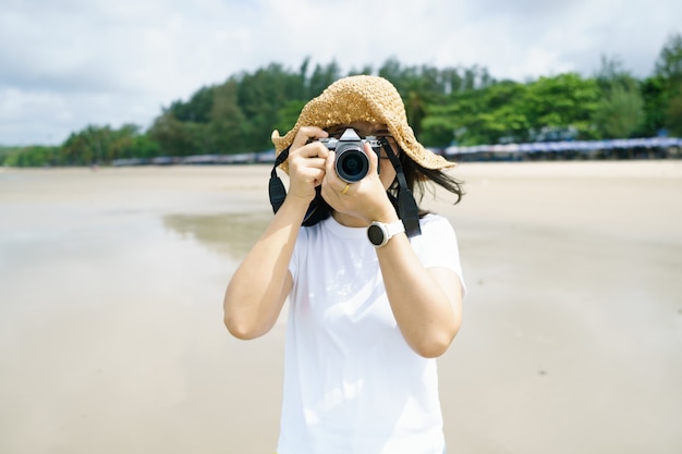 Retrato fotografía de mujer joven con un sombrero usando su cámara sin espejo que cubre su rostro