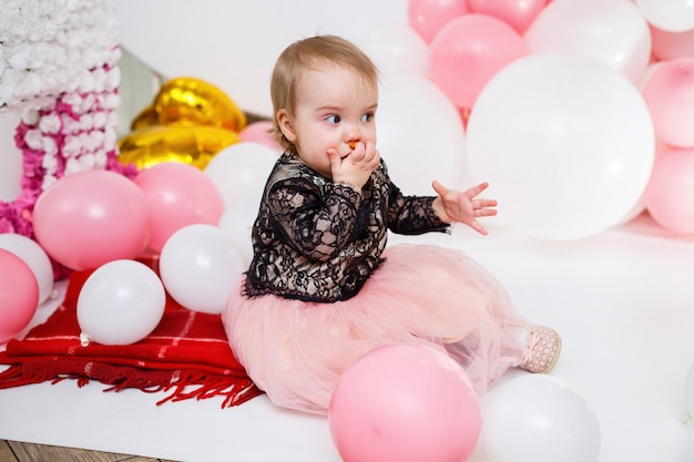 Retrato fotográfico de una cumpleañera de 1 año con un vestido rosa con globos rosas. El niño en la fiesta sonríe, las emociones de los niños. Fiesta de cumpleaños