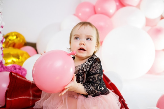 Retrato fotográfico de una cumpleañera de 1 año con un vestido rosa con globos rosas. El niño en la fiesta sonríe, las emociones de los niños. Fiesta de cumpleaños