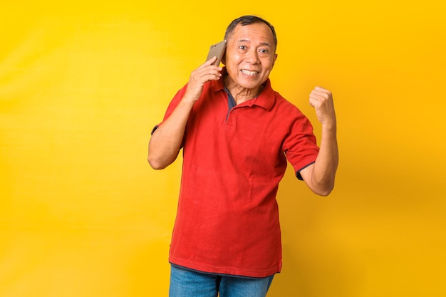 Retrato fotográfico de um velho alegre asiático comemorando a vitória ligando para o telefone em uma mão isolada o