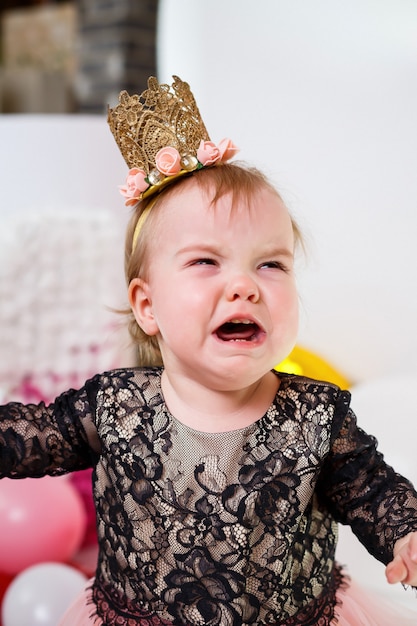 Retrato fotográfico de uma aniversariante de 1 ano em um vestido rosa com balões cor de rosa. a criança chora no feriado, as emoções das crianças. menina chorando