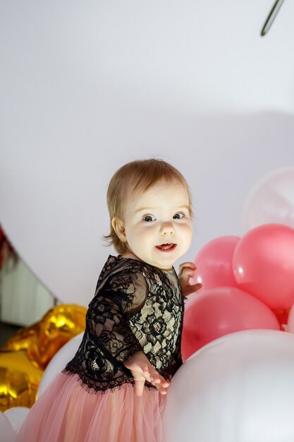 Retrato fotográfico de uma aniversariante de 1 ano em um vestido rosa com balões cor de rosa. a criança no feriado sorri, as emoções das crianças. festa de aniversário