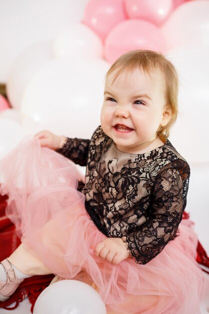 Retrato fotográfico de uma aniversariante de 1 ano em um vestido rosa com balões cor de rosa. A criança no feriado sorri, as emoções das crianças. Festa de aniversário