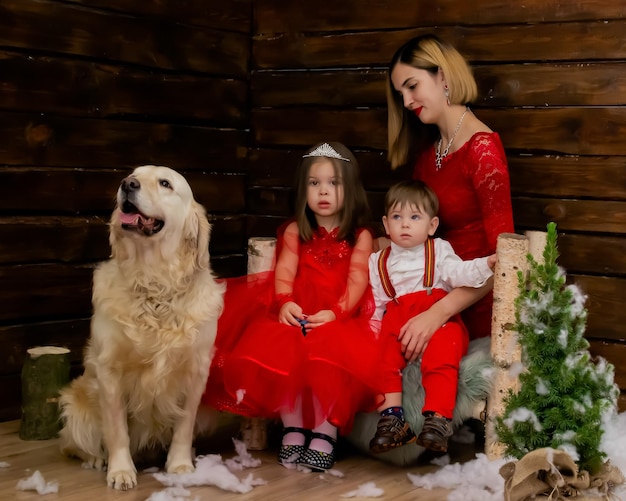 Retrato fotográfico familiarMamá y sus dos hijos y un perro blanco vestido de rojo celebran la Navidad