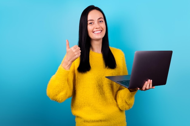 Retrato fotográfico menina bonitinha segura o polegar do netbook para cima novo software legal vestido suéter amarelo na moda