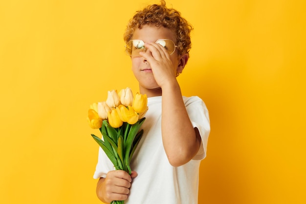 Retrato fotográfico menino encaracolado com um buquê de flores amarelas cor de fundo inalterada