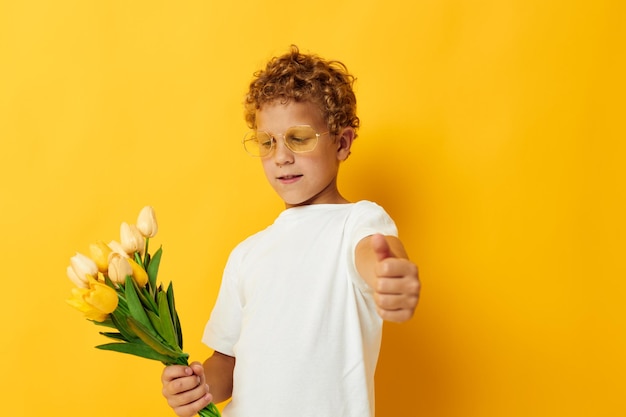 Retrato fotográfico menino encaracolado segurando um buquê de flores um presente fundo amarelo inalterado