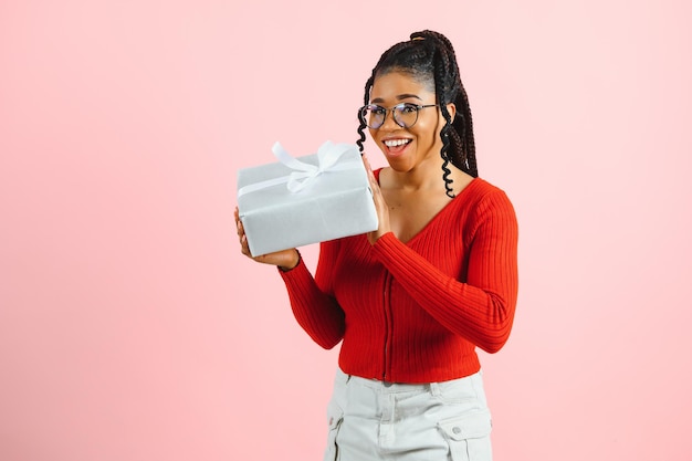 Retrato fotográfico de una mujer emocionada sosteniendo una caja de regalo en dos manos aislada en un fondo de color rosa pastel