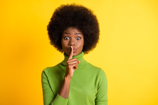 Retrato fotográfico de mujer morena tocando los labios pidiendo silencio aislado sobre fondo de color amarillo vivo