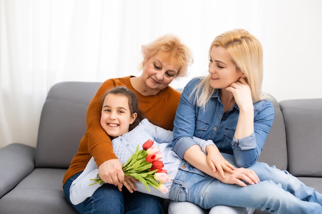 Retrato fotográfico de la nieta felicitando a la abuela dando un ramo de tulipanes sentado cerca de mamá.