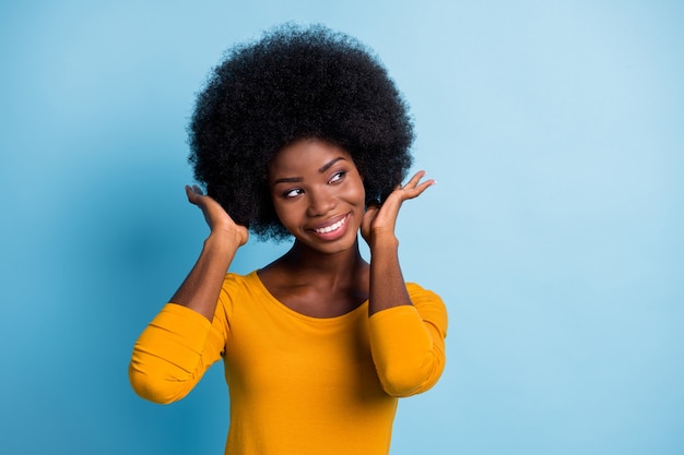 Retrato fotográfico de niña de piel negra tocando el cabello rizado mirando el espacio vacío aislado sobre fondo de color azul brillante