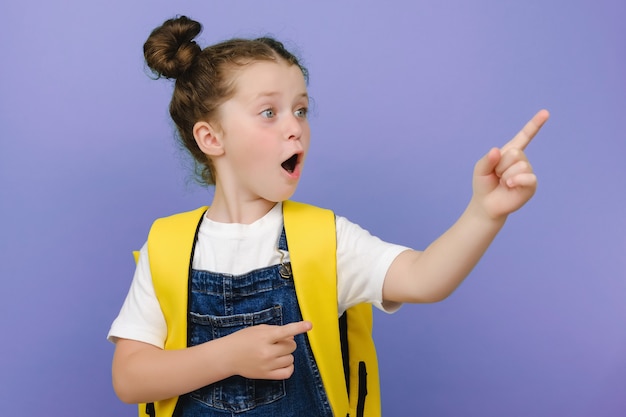 Retrato fotográfico de la pequeña morena con gafas apuntando al espacio en blanco en la mano riendo aislado sobre fondo de color violeta brillante