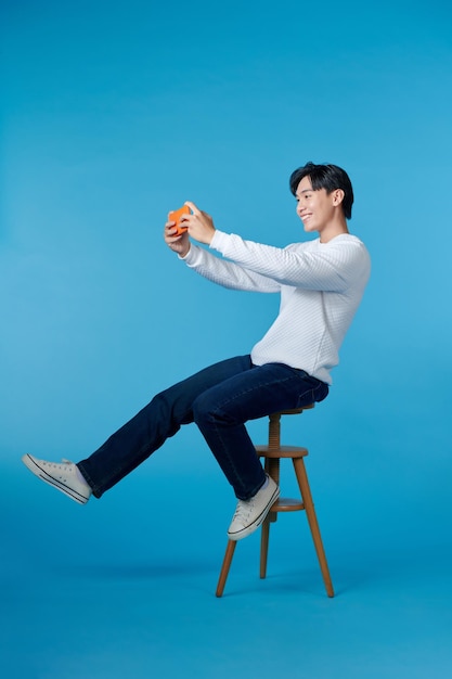 Retrato fotográfico de un tipo asombrado, emocionado, jugando a juegos en su teléfono inteligente, loco, aislado sobre un fondo azul.