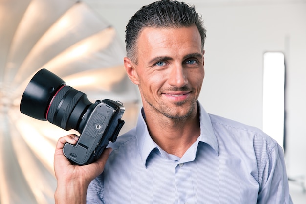 Retrato de un fotógrafo feliz sosteniendo la cámara en el estudio