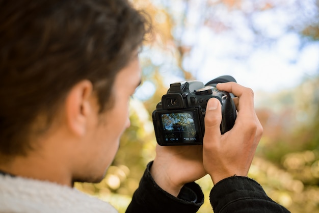 Foto retrato de un fotógrafo masculino filmando video en modo de visualización en vivo del hermoso bosque otoñal