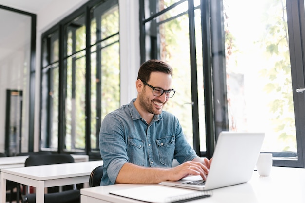 Foto retrato del freelancer joven feliz que usa la computadora portátil.