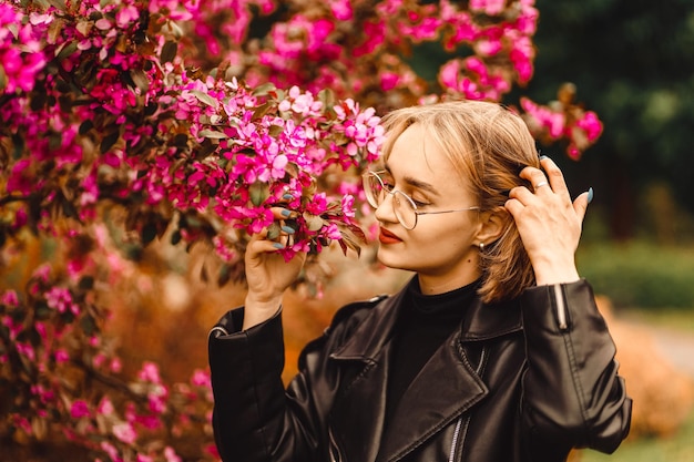 Retrato fresco y brillante de una joven rubia feliz vestida de negro en el fondo de un árbol de flores rosas