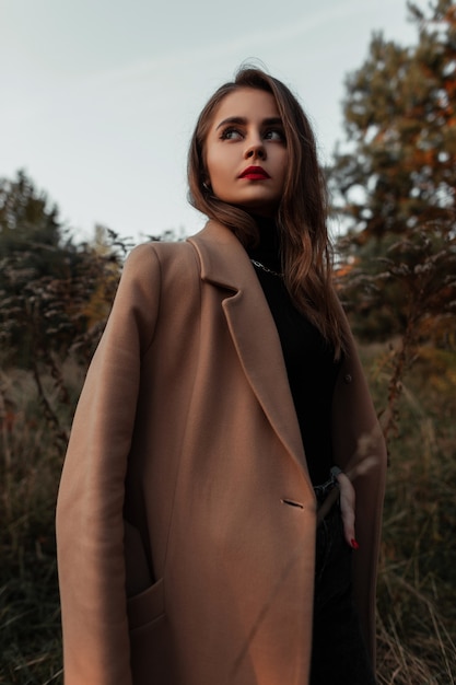 Foto retrato fresco e elegante de uma modelo de uma linda jovem com um elegante casaco bege na natureza