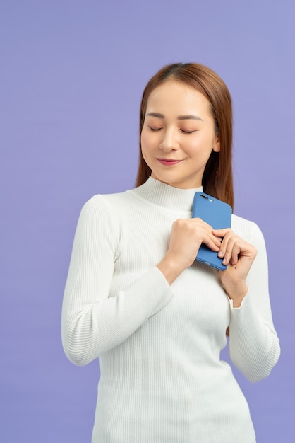 Retrato frontal de uma jovem sorridente usando telefone celular contra a parede violeta