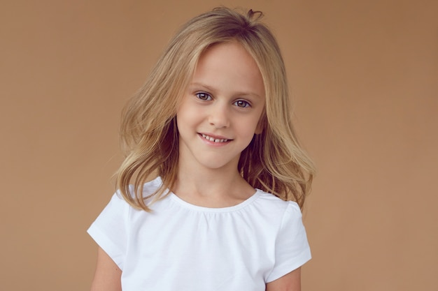 Retrato frontal de uma menina bonita com cabelos loiros ondulados, vestida com roupas brancas