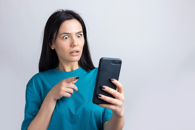 Retrato frontal de una joven mujer sonriente mediante teléfono móvil contra un fondo gris