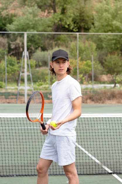 Retrato frontal de un joven tenista atlético con una gorra negra mirando su c y esperando para jugar en la cancha verde