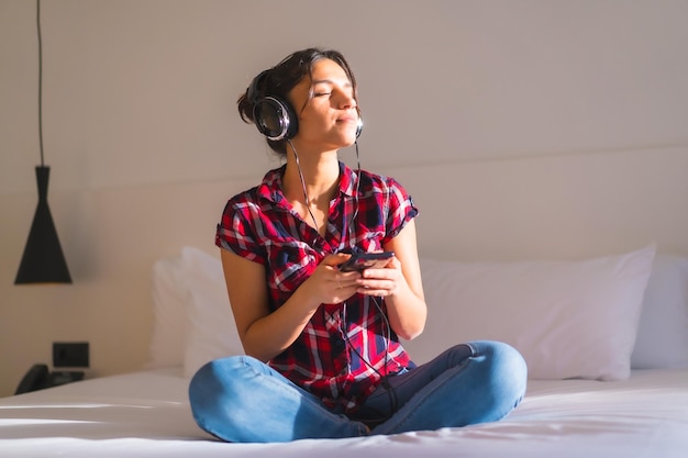 Foto retrato frontal de una mujer relajada escuchando música sentada en una cama cómoda