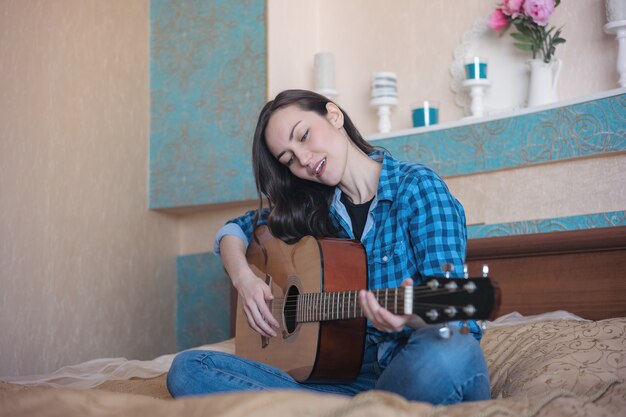 Retrato frontal de una niña con una guitarra acústica en la cama