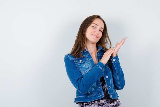 Retrato de frotar las palmas juntas en chaqueta de mezclilla, vestido y mirando satisfecho vista frontal