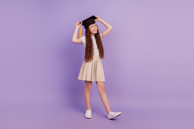 Retrato de funky adorable lindo estudiante chica manos sombrero de graduación sobre fondo púrpura