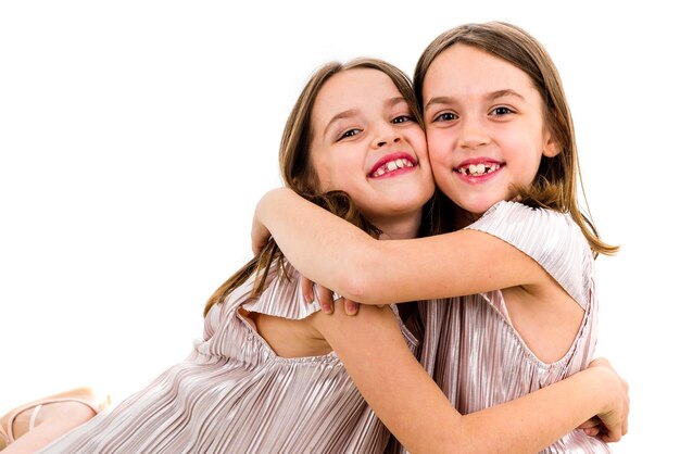 Retrato de gemelos sonrientes abrazándose contra un fondo blanco.