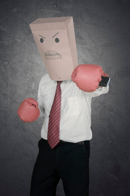 Foto retrato de gerente masculino con una bolsa de papel en la cabeza, con guantes de boxeo y golpeando a la cámara