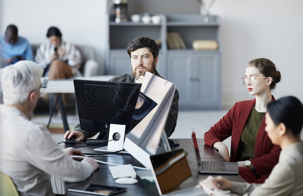 Retrato de gerente de negocios barbudo escuchando a sus colegas durante la reunión en la mesa en el interior de la oficina blanca, espacio de copia