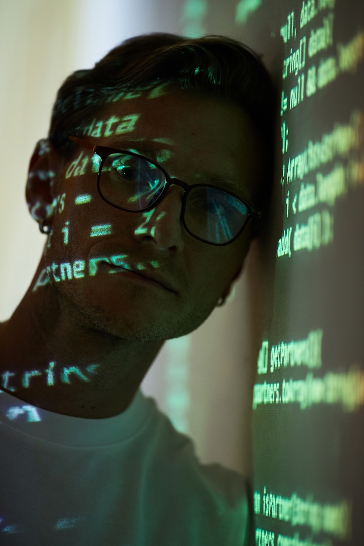 Foto retrato de gerente de ti en anteojos mirando a la cámara mientras está de pie cerca de la pizarra con código de computadora en él