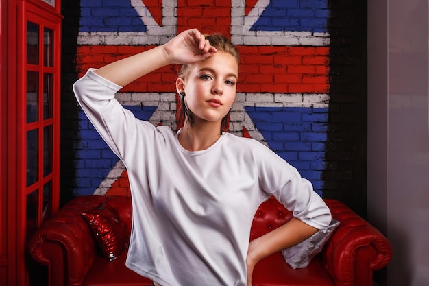 Retrato glamoroso de moda de um modelo de menina com suéter branco no fundo da parede com uma bandeira britânica