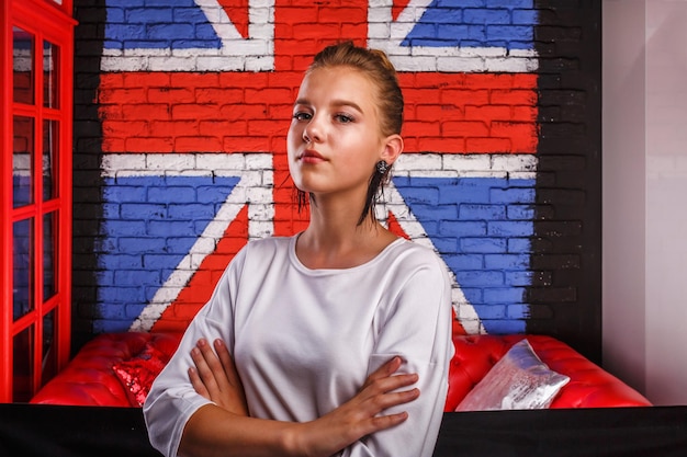 Retrato glamoroso de moda de um modelo de menina com suéter branco no fundo da parede com uma bandeira britânica