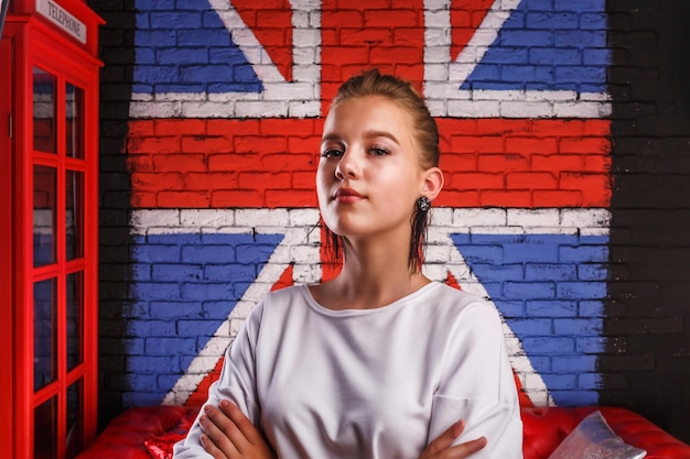 Retrato glamoroso de moda de um modelo de menina com suéter branco no fundo da parede com uma bandeira britânica