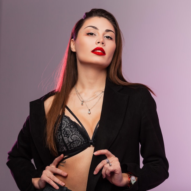 Retrato glamoroso jovem mulher bonita com lábios vermelhos sensuais com cabelo castanho longo chique na cueca de renda em casaco preto elegante no estúdio com luz brilhante. Modelo de garota muito linda e sensual.