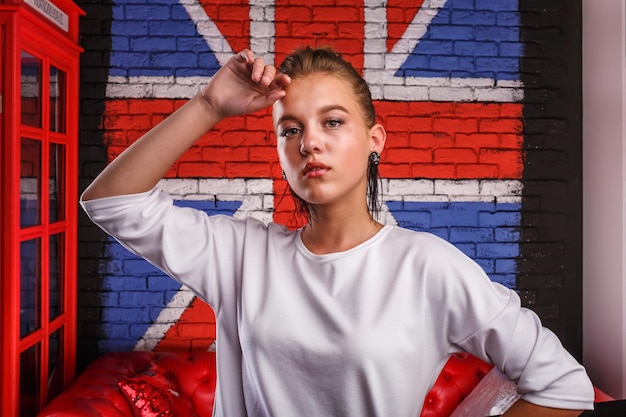 Retrato glamoroso de moda de una modelo de niña con suéter blanco en el fondo de la pared con una bandera británica