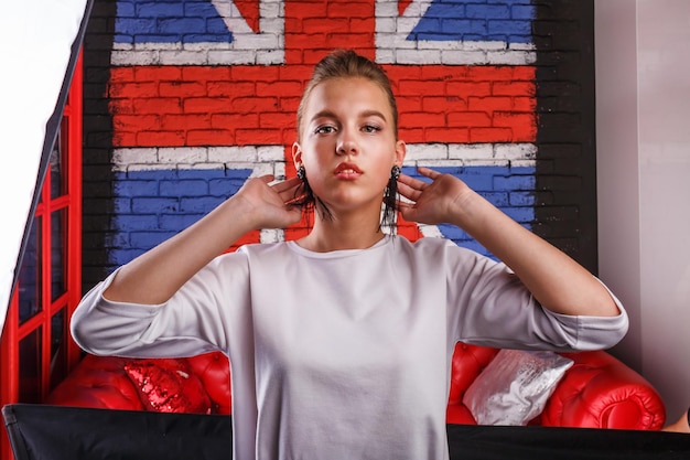 Foto retrato glamoroso de moda de una modelo de niña con suéter blanco en el fondo de la pared con una bandera británica