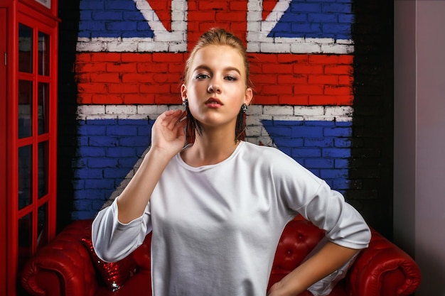 Retrato glamoroso de moda de una modelo de niña con suéter blanco en el fondo de la pared con una bandera británica