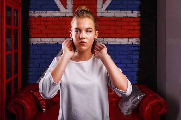 Retrato glamoroso de moda de una modelo de niña con suéter blanco en el fondo de la pared con una bandera británica