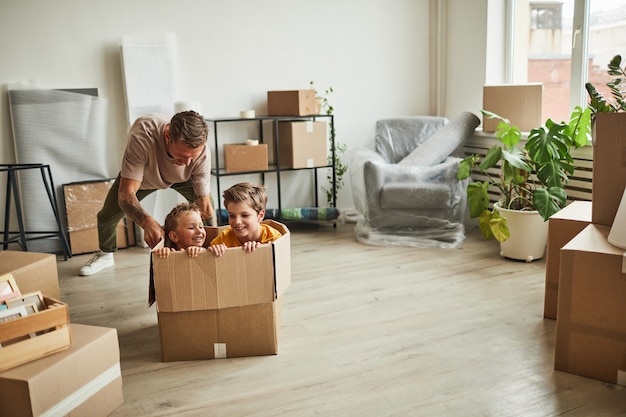 Retrato de gran angular de dos niños jugando en una gran caja de cartón mientras la familia se muda a la nueva casa ...