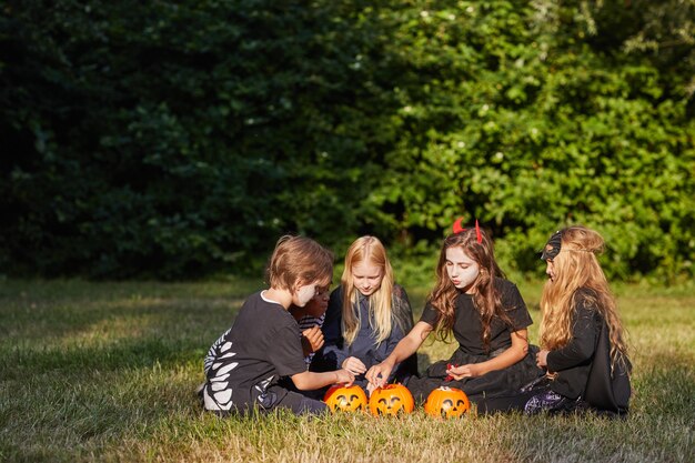 Retrato de gran angular de un grupo multiétnico de niños comiendo dulces en Halloween al aire libre mientras usan disfraces, espacio de copia