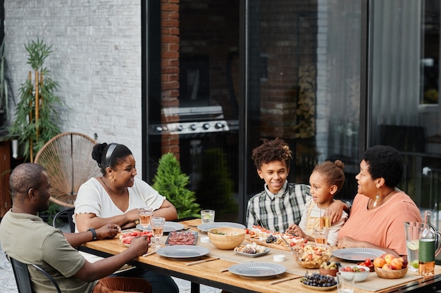 Retrato de gran familia afroamericana disfrutando de una cena juntos al aire libre y sonriendo espacio de copia